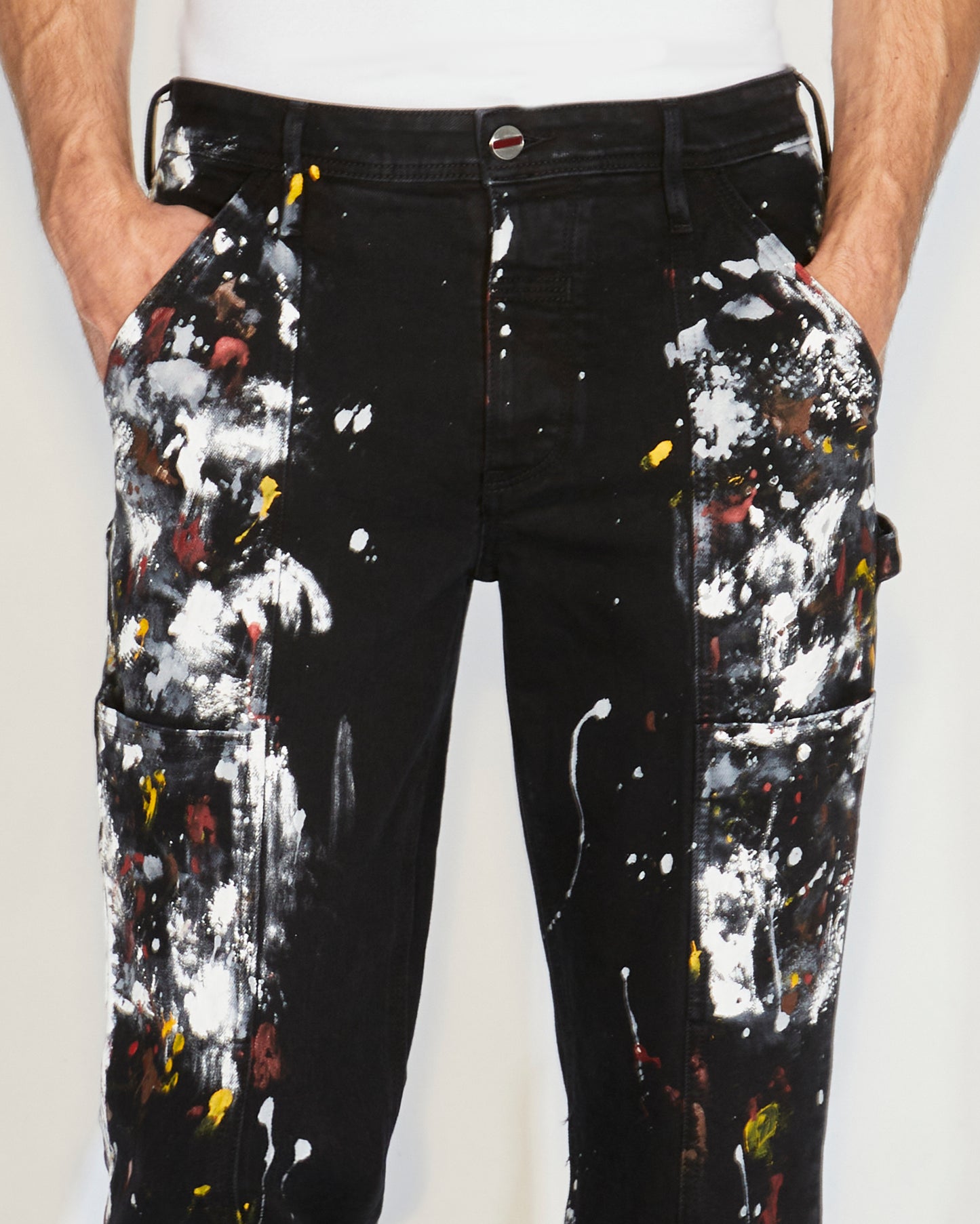 Man standing wearing black pants with paint splatter and a white tee and black shoes